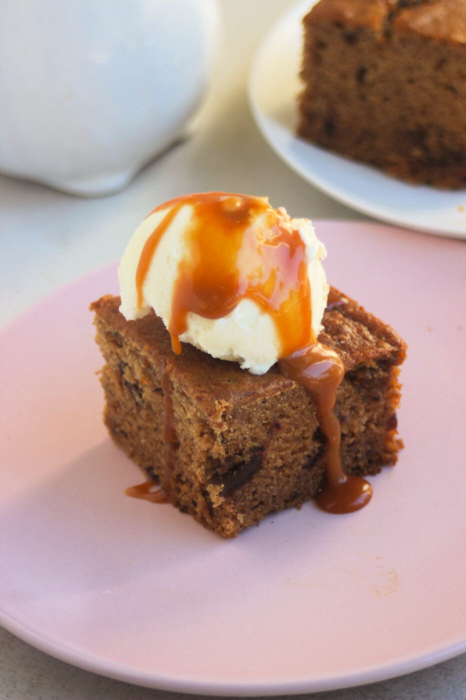 Portion of date cake topped with a scoop of ice cream and caramel sauce on a pink plate.