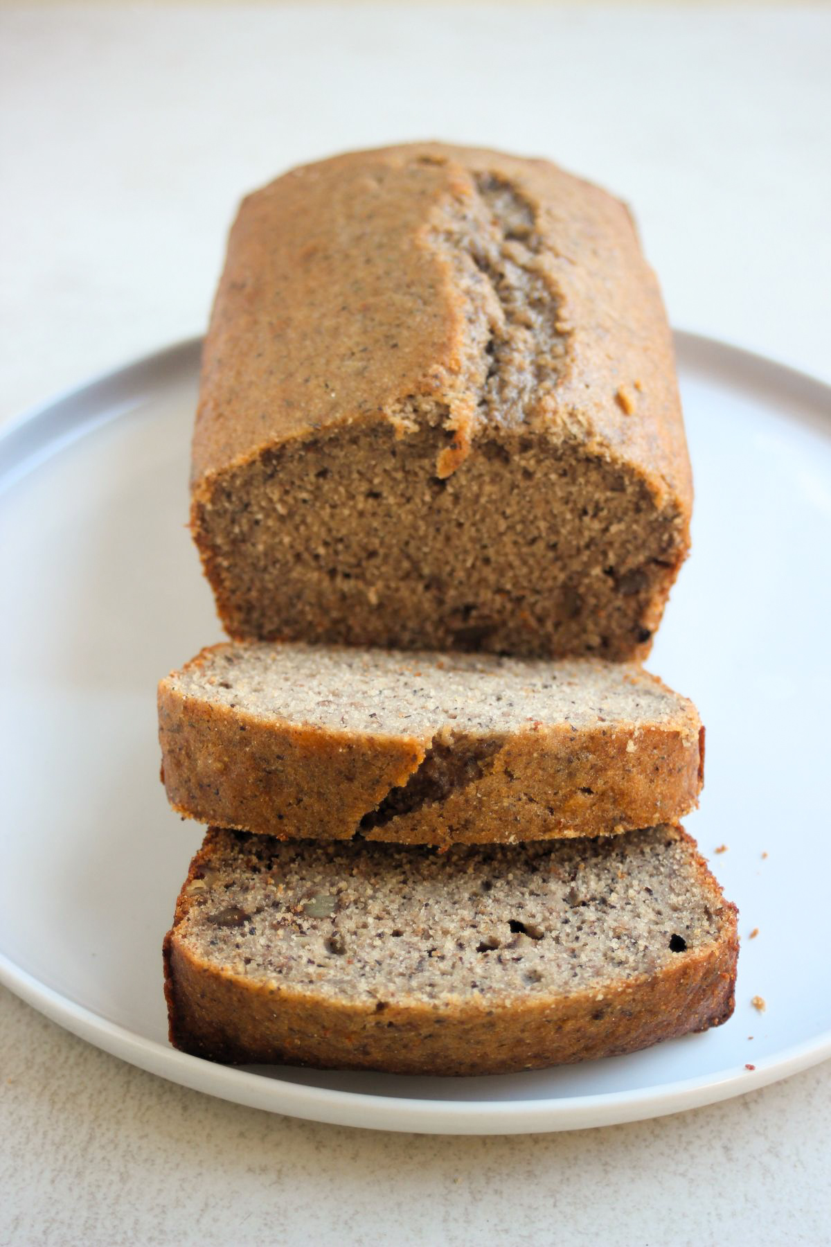 Front view of banana loaf cake and two slices of it on a white plate.