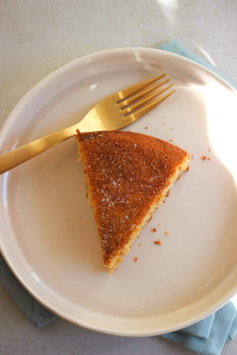 A portion of cinnamon teacake on a cream-coloured plate, and a golden fork seen from above.