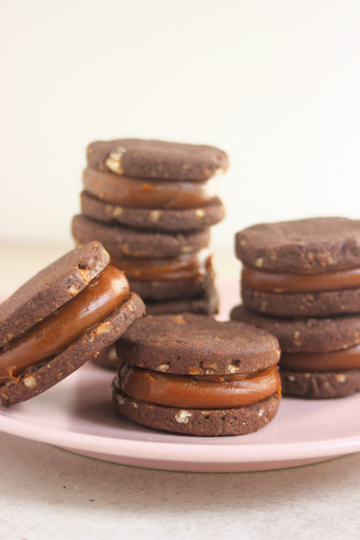 An alfajor resting on another alfajor on a pink plate. Two stacks of alfajores bekind.