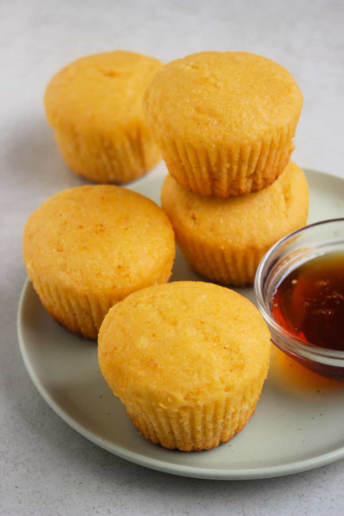 Cornbread muffins and a dip of honey on an aqua-green plate. One muffin is stack on another muffin.