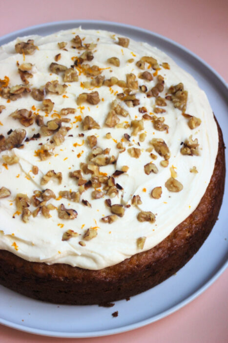 Carrot cake with cream cheese frosting and chopped walnuts on a white plate.