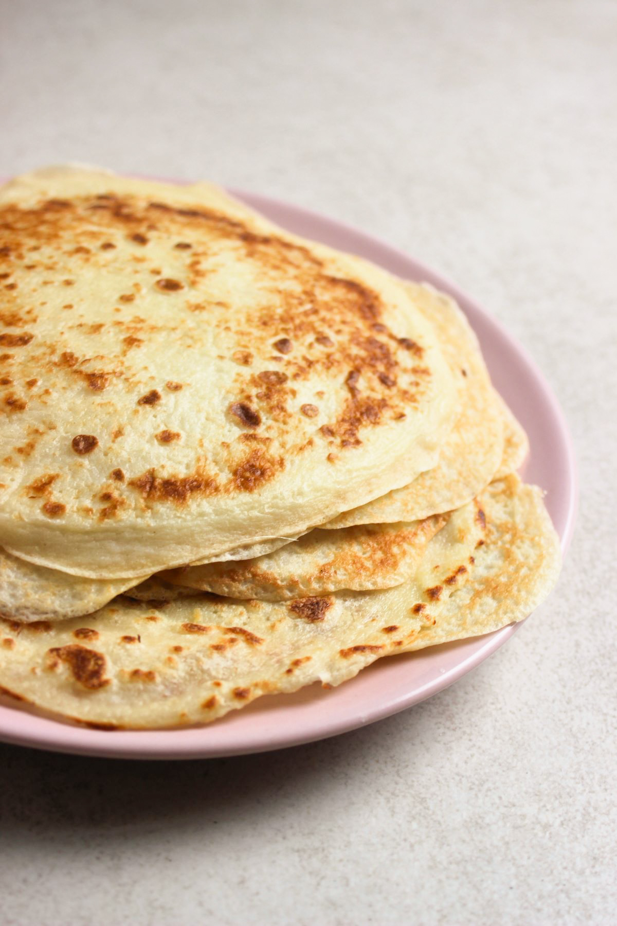 Stacked crepes on a pink plate on a white surface.