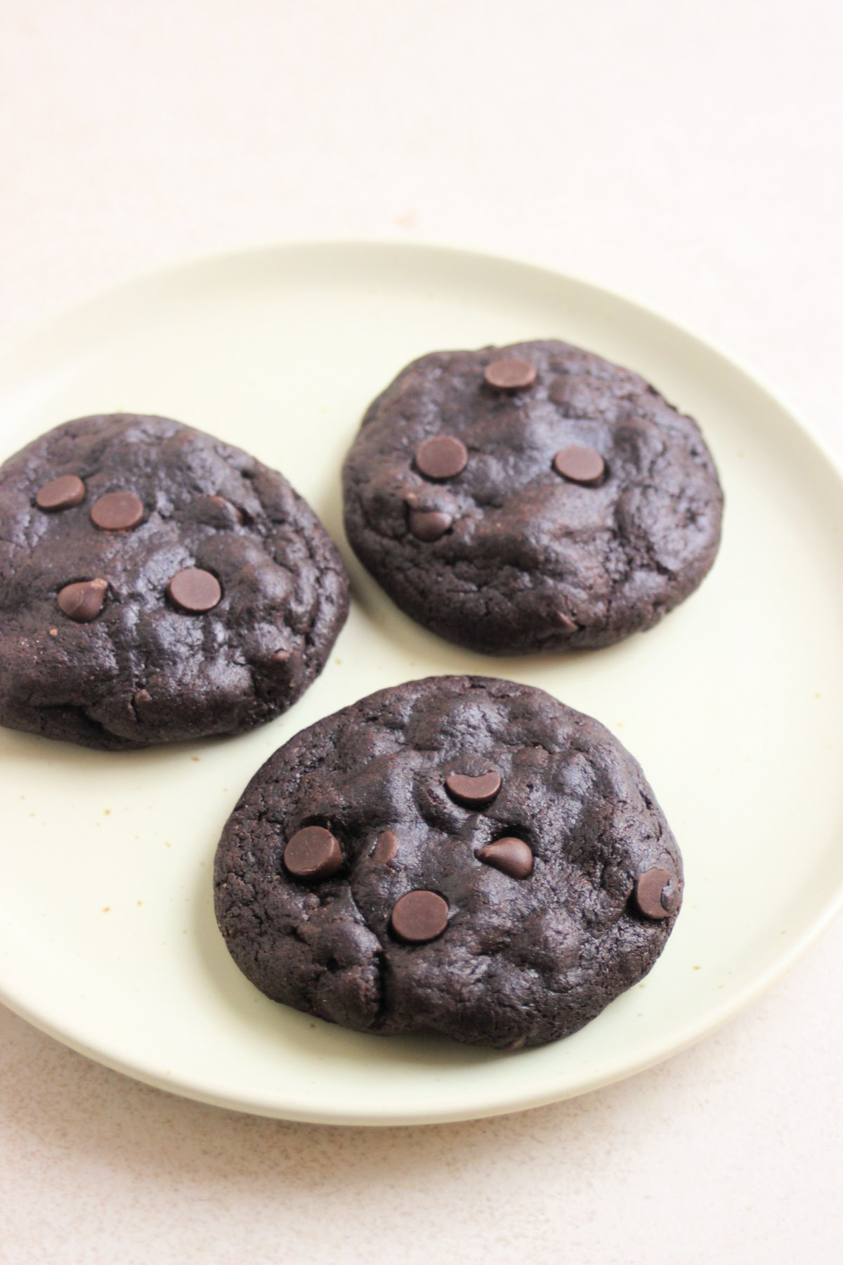Three double chocolate chip cookies on an aqua green plate.