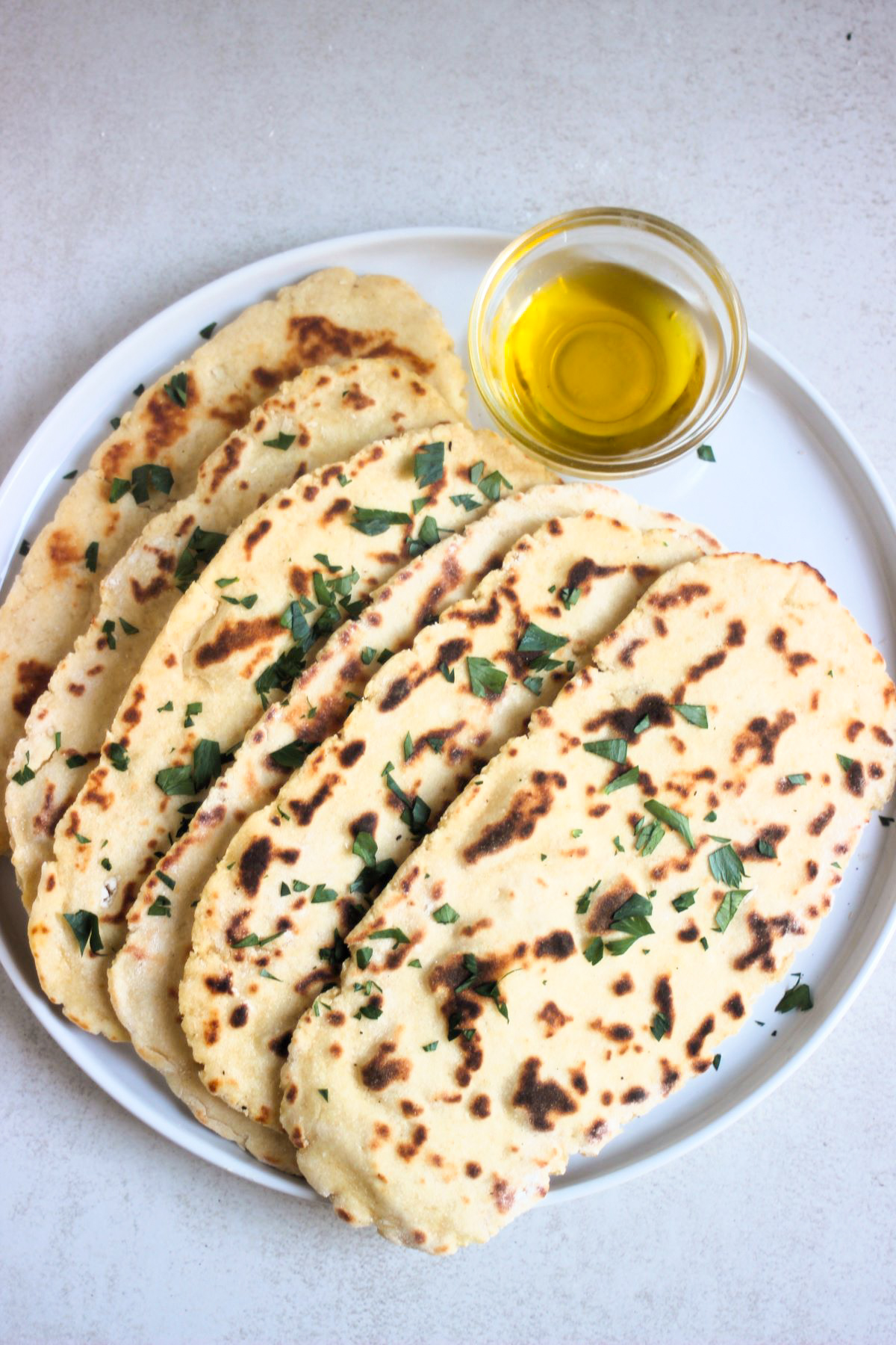 Flatbread plate with chopped fresh parsley on a white plate and a dip of olive oil.