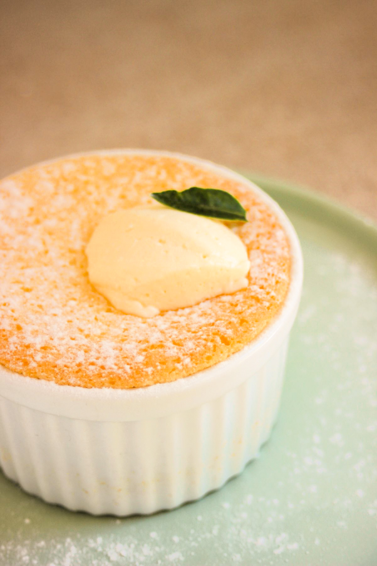 White ramekin with lemon pudding cake and whipped cream on an aqua green plate.