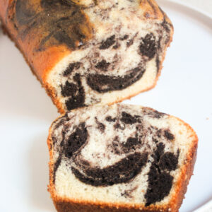 Marble loaf cake and a slice of it on a white plate.