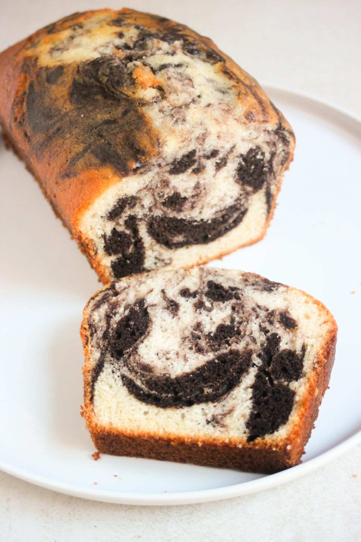 Marble loaf cake and a slice of it on a white plate.