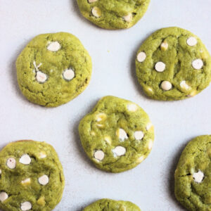 Matcha cookies with white chocolate chips on a white surface seen from above.