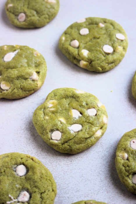 Matcha cookies with white chocolate chips on a white surface.