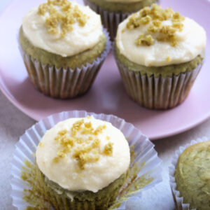 Matcha cupcake with the liner open. Behind, more cupcakes on a pink plate.