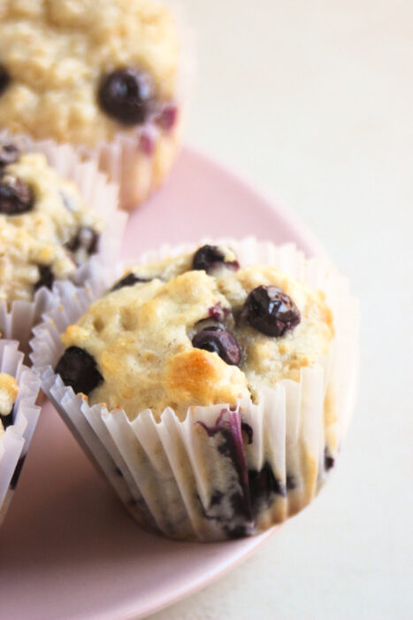 Blueberry muffin with a liner on a pink plate.