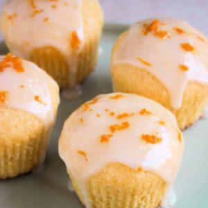 Orange coconut muffins with icing on an aqua-green plate.