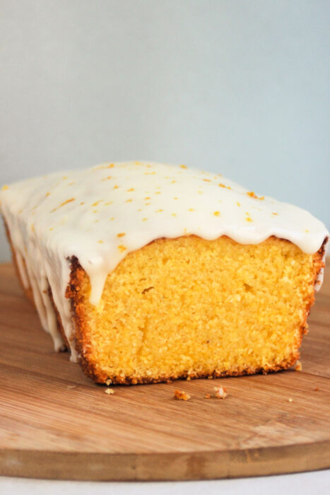 Orange polenta loaf cake with icing on a wooden table.
