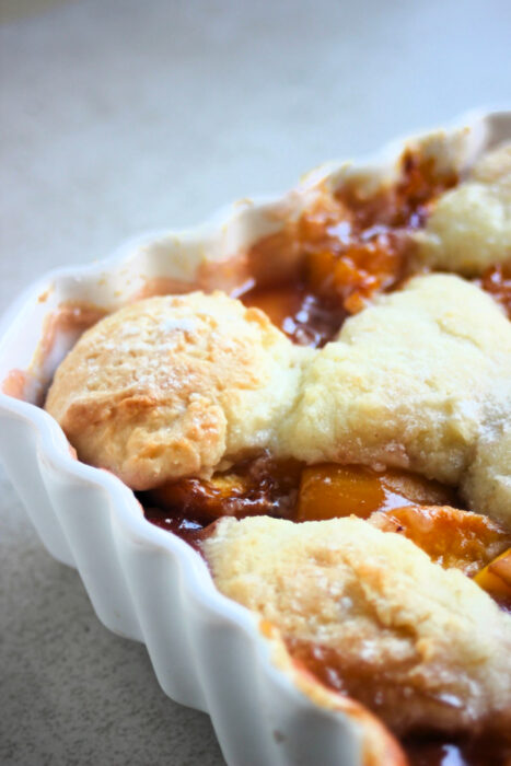 Partial close view of a baking dish with peach cobbler.