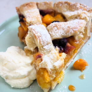 Peach pie portion with whipped cream on an aqua-green plate.