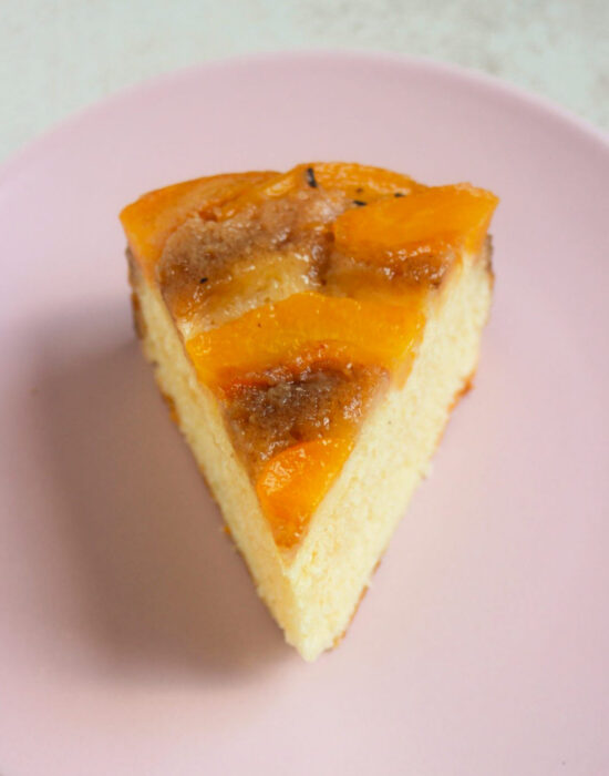 A portion of peach upside down cake on a pink plate.