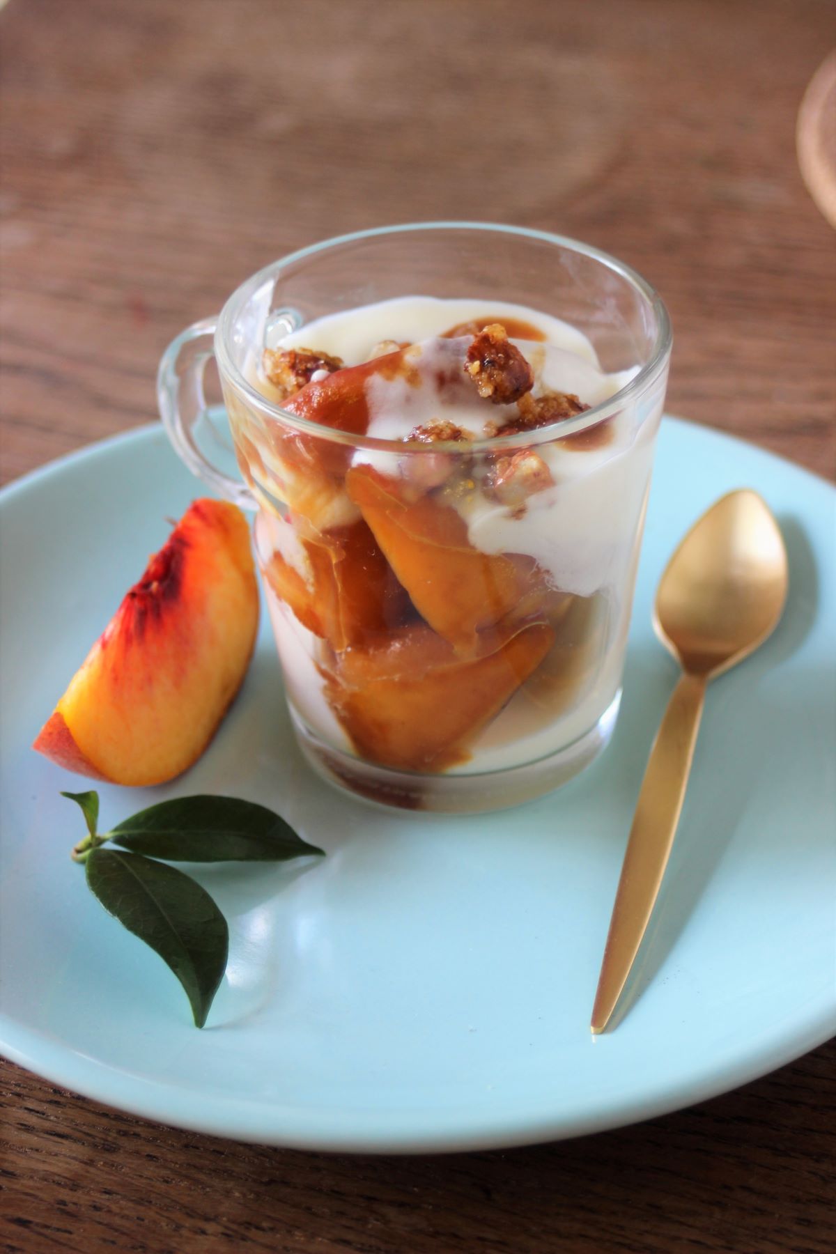 Glass cup with cream, peaches, and caramelized almonds on a light blue plate.