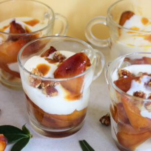 Four peach yogurt trifles in glass cups on a white surface. Green leaves on the sides.
