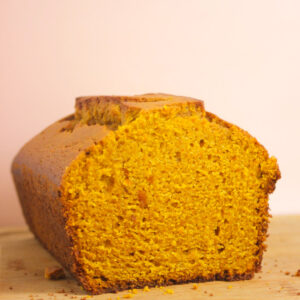 Pumpkin bread on a wooden table. Light pink background.
