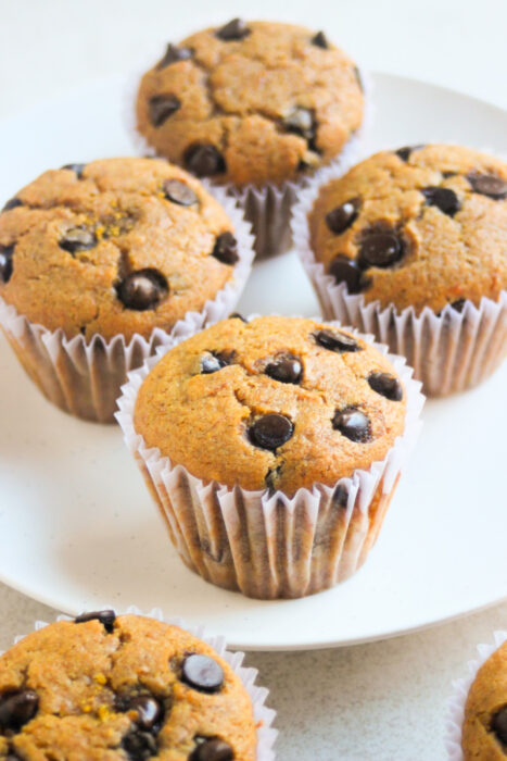 Pumpkin muffins with chocolate chips and liners on a white plate.