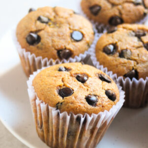 Pumpkin muffins with chocolate chips and liners on a white plate.