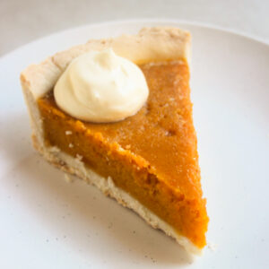 Portion of pumpkin pie en a scoop of whipped cream on a white plate.