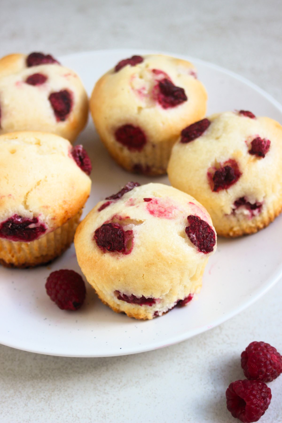 Raspberrie muffins and fresh raspberries on a white plate.