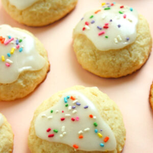 Ricotta cookies with icing and sprinkles on a light orange surface.