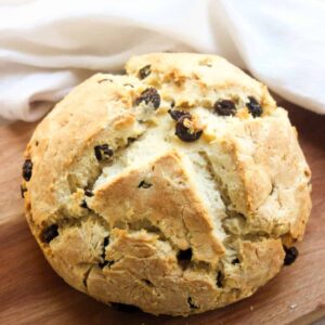Soda bread with raisins on a wooden board. White kitchen towel behind.