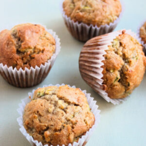 Zucchini muffins with liners on a light grey surface.