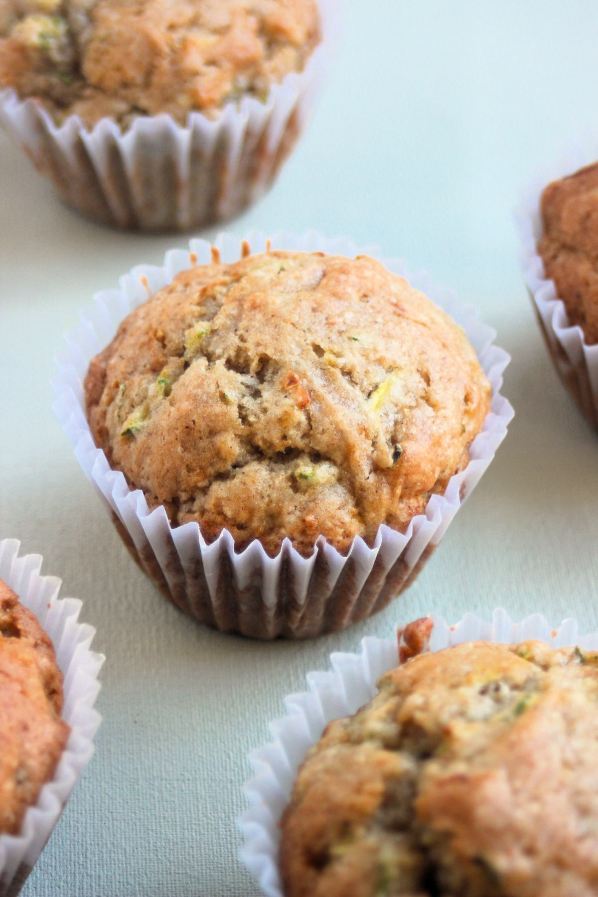 Zucchini muffin with a liner on a grey surface.