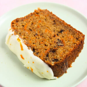 A slice of carrot loaf cake with cream cheese frosting on an aqua-green plate.