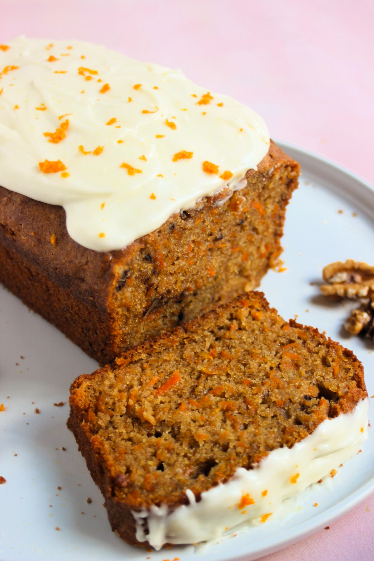 Carrot loaf cake with cream cheese frosting and a slice of it on a white plate.