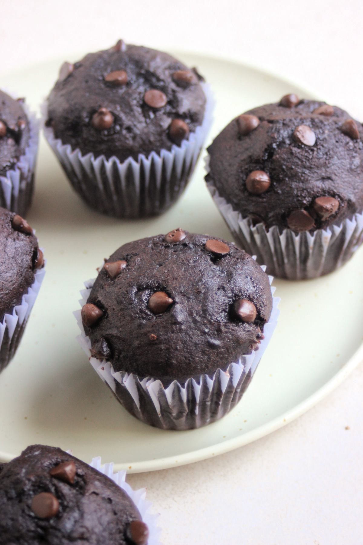 Double chocolate chip muffins with liners on an aqua green plate.