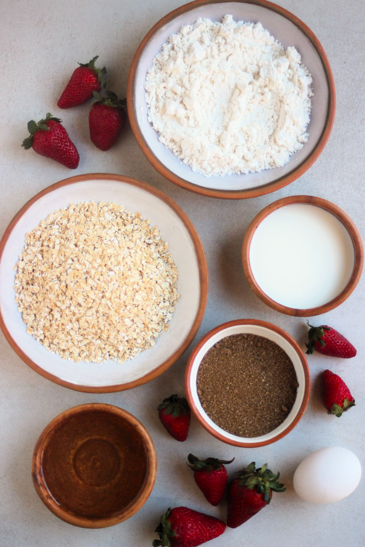 Top view of oatmeal strawberry muffins ingredients on a white surface.
