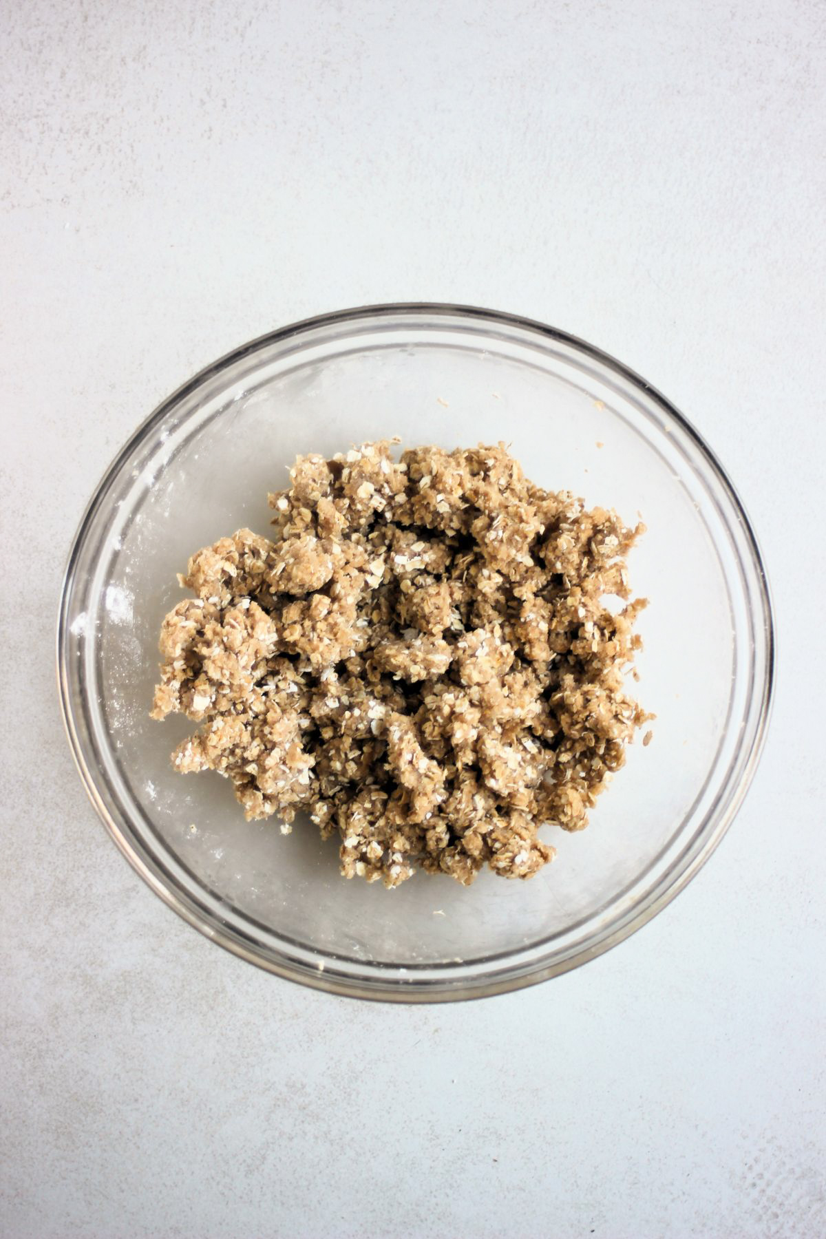 Glass bowl with a light brown crumble that includes oats.