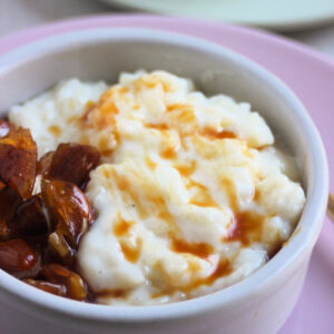 Small bowl with rice pudding, caramel, and praline on a pink plate.
