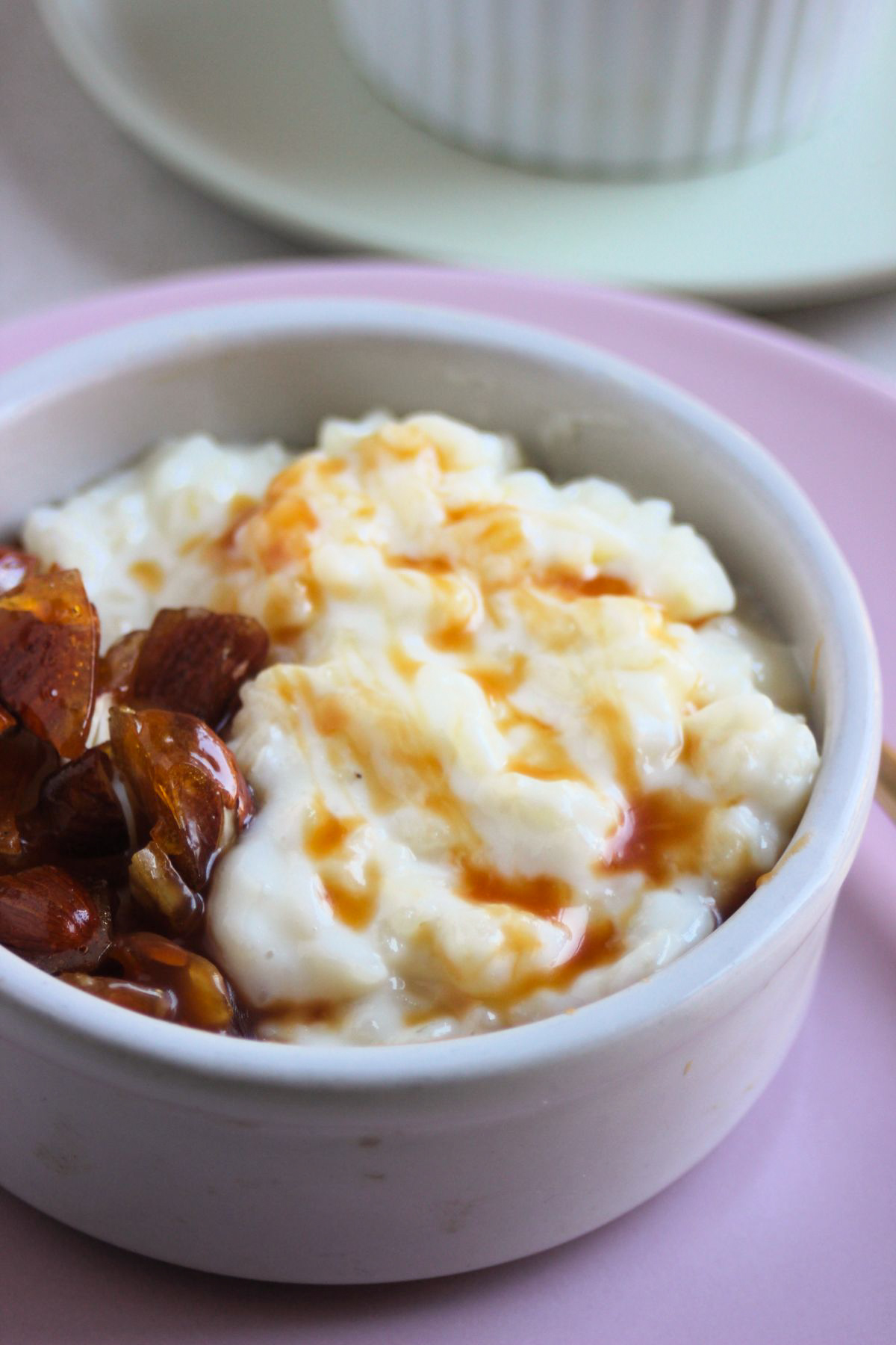 Small bowl with rice pudding, caramel, and praline on a pink plate.
