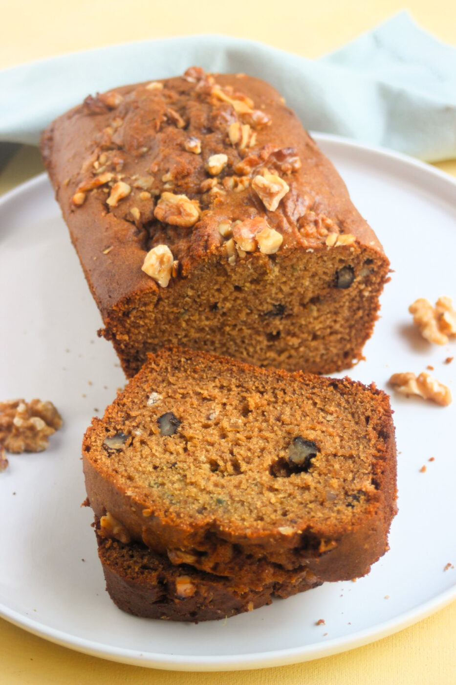 Sweet potato bread with walnuts, with two slices on a white plate. A white napkin behind. Yellow surface.