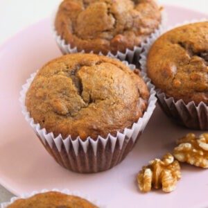 Sweet potato muffins in liners on a pink plate and walnuts beside.
