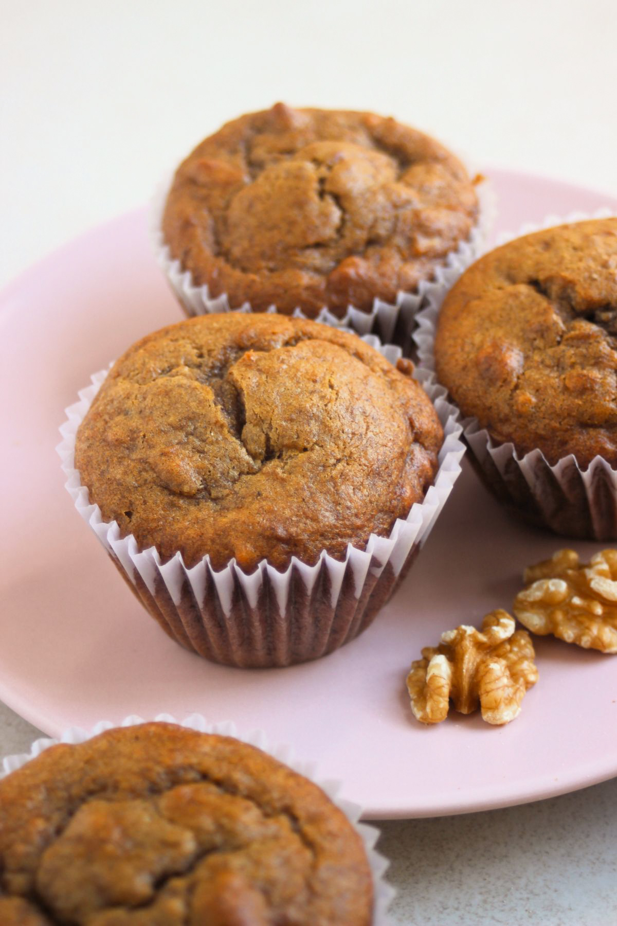 Sweet potato muffins in liners on a pink plate and walnuts beside.