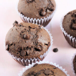 Chocolate buckwheat muffins in liners on a pink surface.