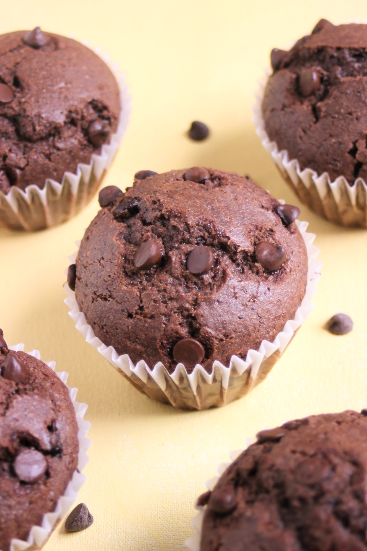 Chocolate buckwheat muffins in liners on a yellow surface.