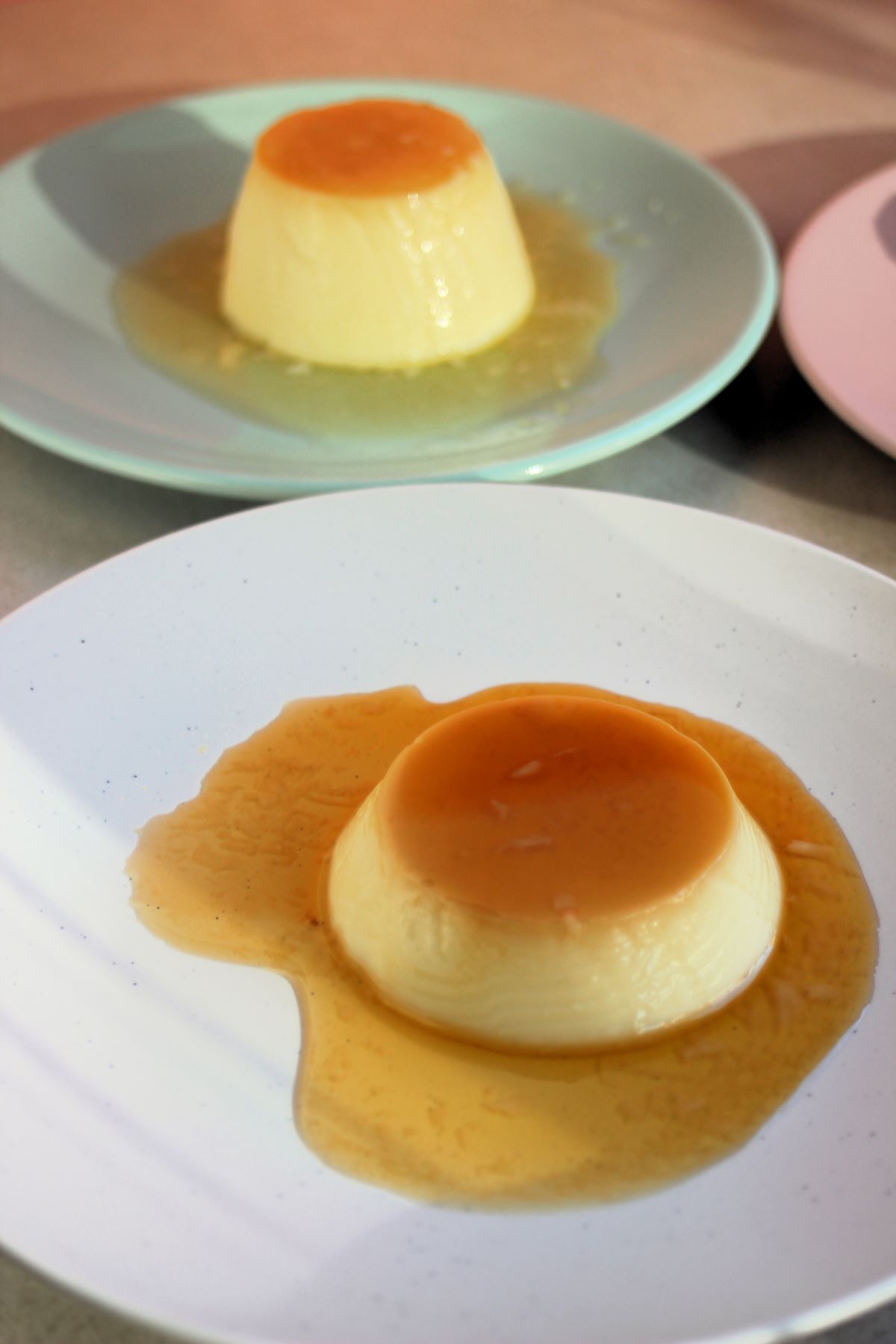 Flan with caramel on a white plate. Another plate with a flan behind.
