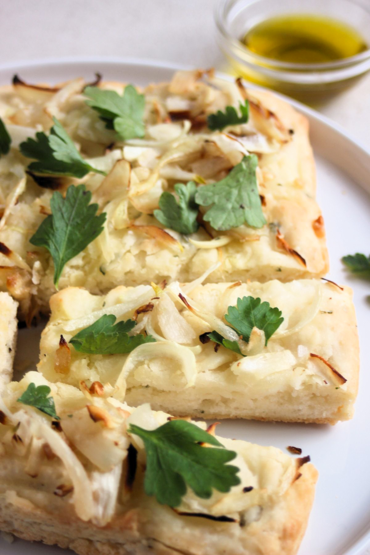 Partial view of onion focaccia sliced on a white plate.