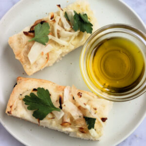 Top view of two onion focaccia slices on a plate and a dip of olive oil.