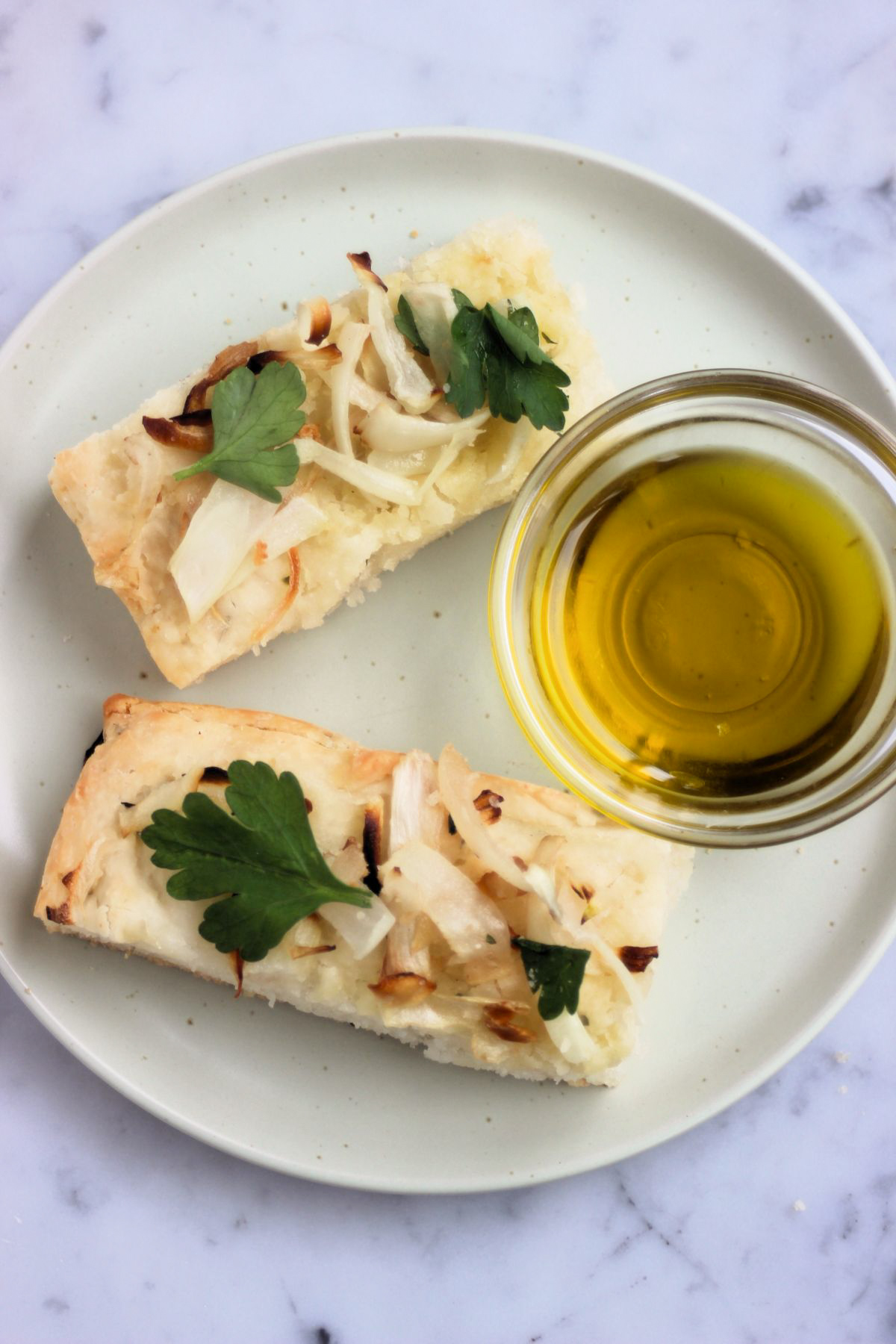 Top view of two onion focaccia slices on a plate and a dip of olive oil.