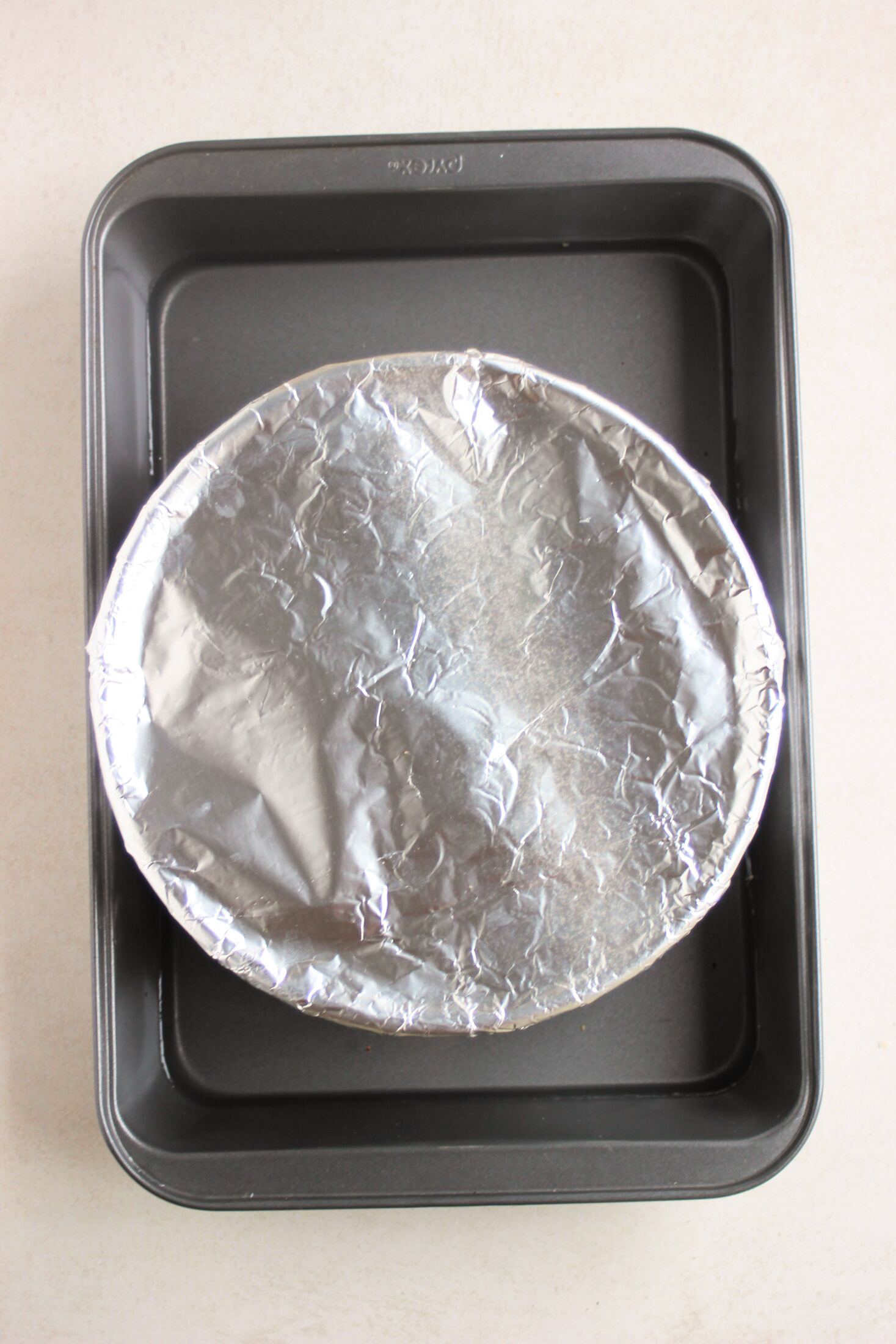 Baking pan with a round mold in it covered with aluminium paper.